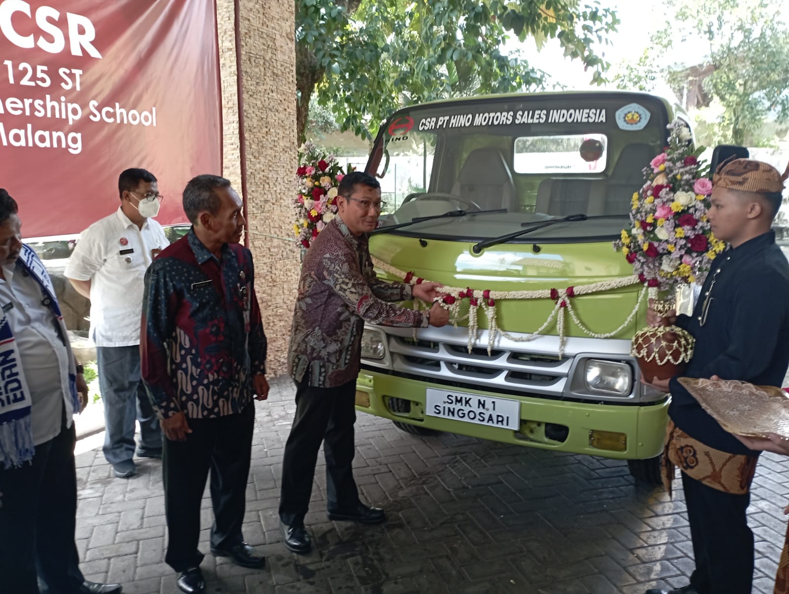 After Sales Director PT Hino Motors Sales Indonesia (HMSI), Irwan Supriyono memotong rangkaian bunga sebagai tanda penyerahan secara resmi bantuan kepada SMKN 1 Singosari